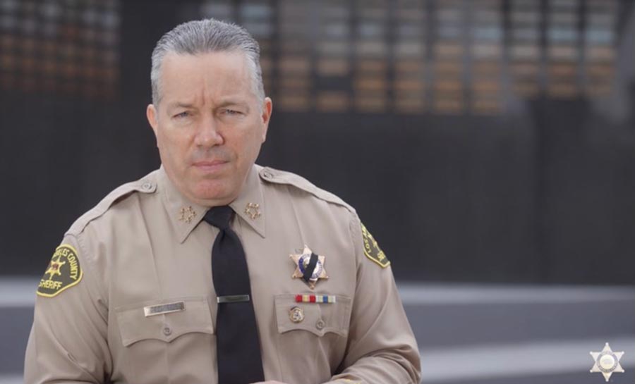 Picture of Sheriff Villanueva in uniform stading infront of the LASD Memorial Wall addressing the camera.