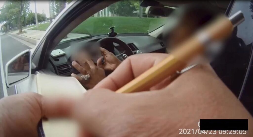 Still image from Body Camera Footage of Deputy writing ticket to a woman inside a car. The Woman is holding up her phone showing the Deputy something on the screen. The image details have been blured to protect the woman's personal information and Identity.