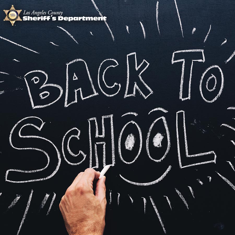 image of a hand writing on a chalk board, the board reads "BACK TO SCHOOL" and has a smile under the two o in the word "School".