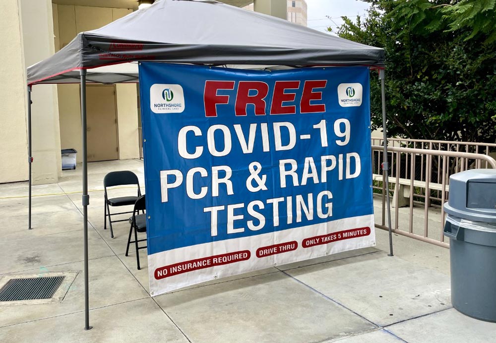 Tent and banner that reads. FREE Covid 19, pcr and rapid testing. The tent is on long legs with a dark blue canopy, the banner is blue. with white type.