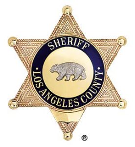image of the Sheriff's Badge. Gold 6 point star. blue circular band with gold letters that reads "Sheriff, Los Angeles County". An engraving of a Bear is in the center.