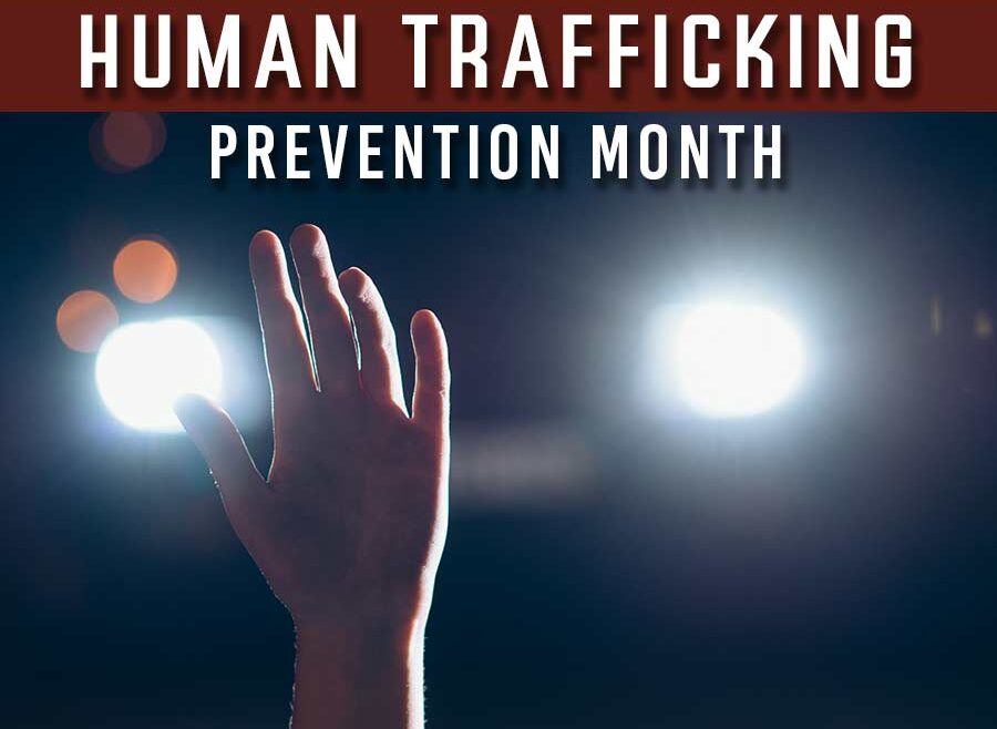 image of a person holding up thier hand calling for help .There are lights from an on comming car driving towards the viewer. Text accross the top reads National Human Trafficking prevention Month.