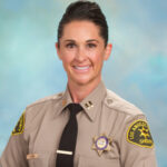 Capt. jodi hutak is dressed in a black tie and seated infront of a blue background. In uniform