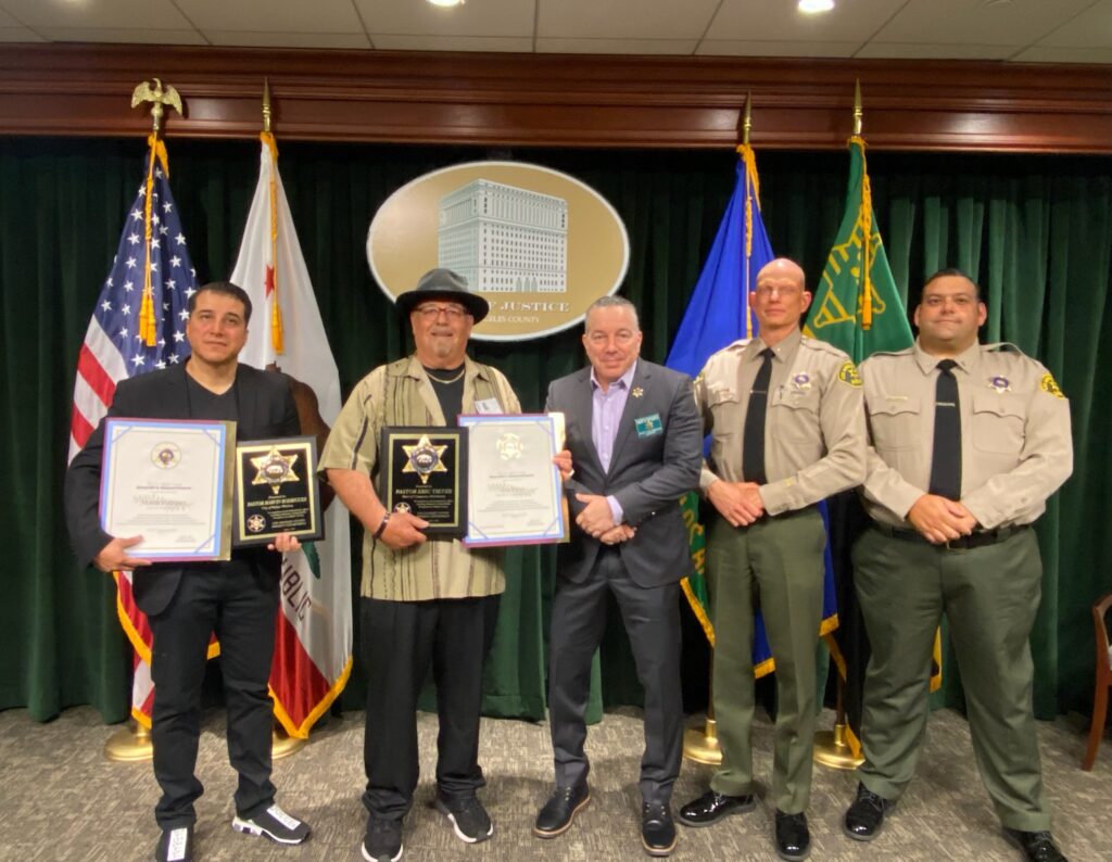 image of award recipeints standing next to the sheriff. Two pastors and the sheriff is next to a podium.