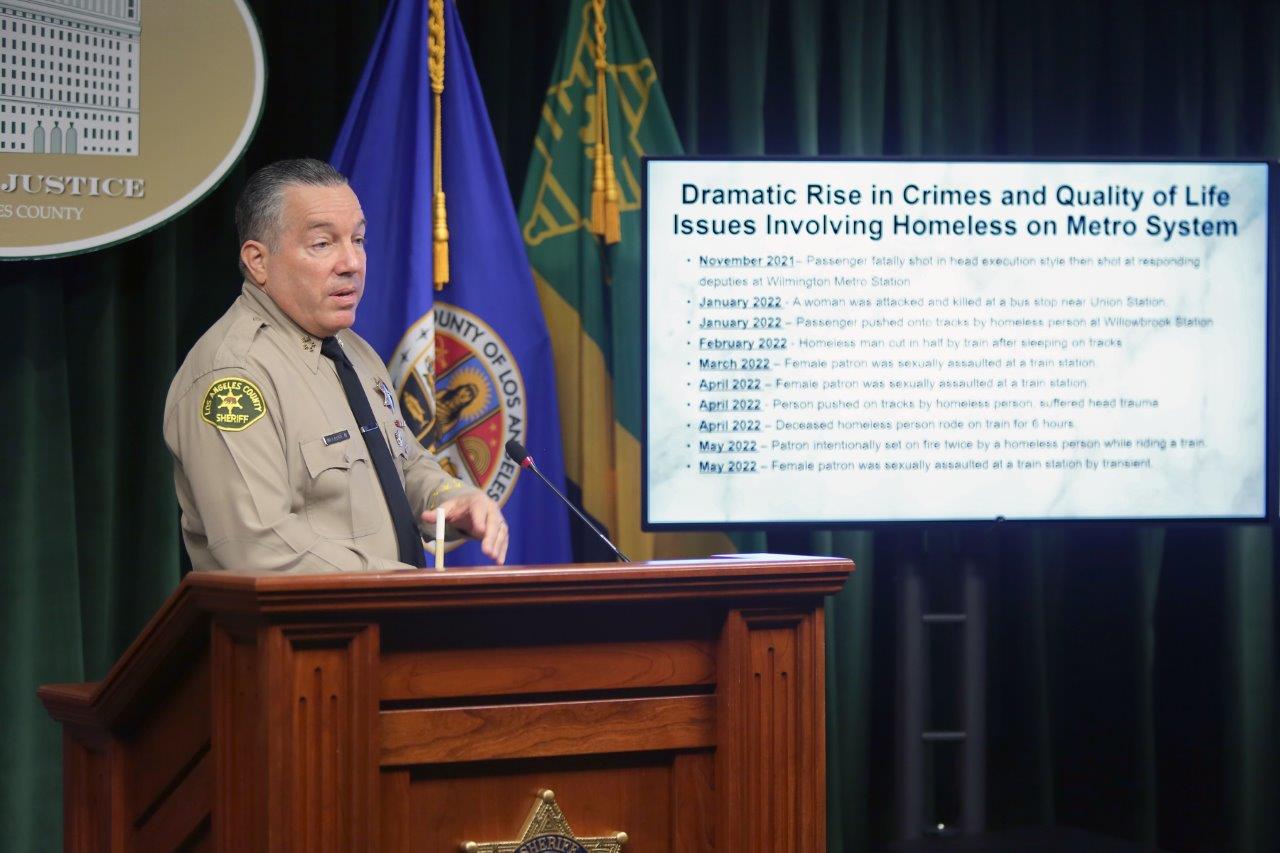 Sheriff Villanueva is standing at a podium infront of a TV that reads. "Dramatic Rise in crimes. Quality of life issues involving homlessnes on the Metro.