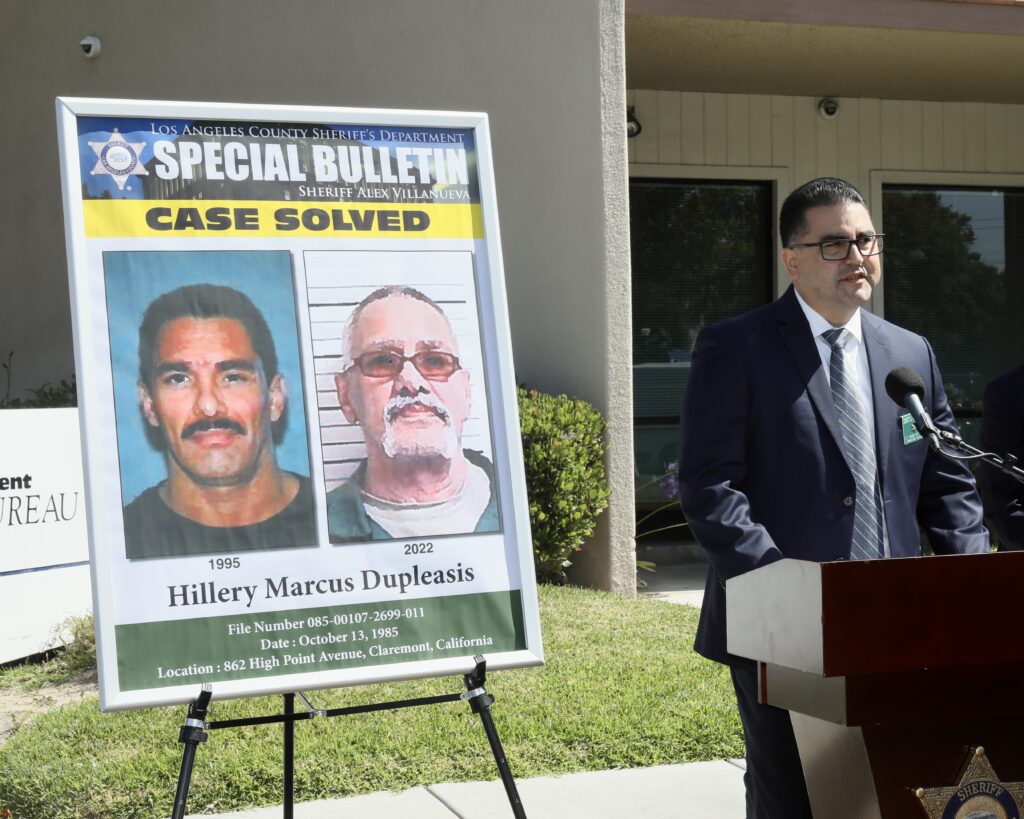 Image of LASD Leutenant standing at a podium with a flyer that reads Case Solved.