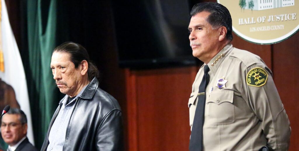 Actor Danny Trejo is standing at a podium with Sheriff Luna Standing near by.
