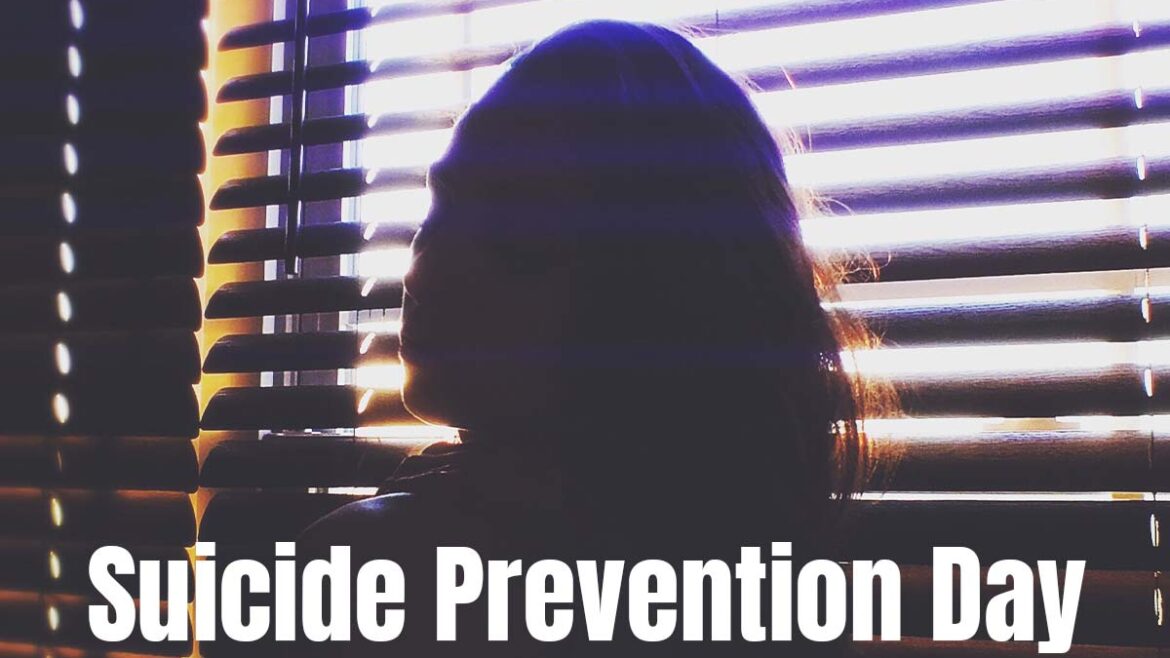 Suicide Prevention Day; You're not alone. Text over an image of a person with long hair sitting in front of partially open blinds. the person is back light so you only see a silhouette.