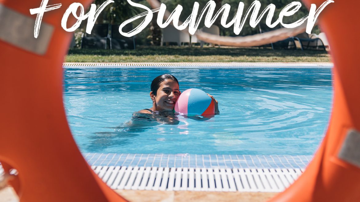 Pool Safety Tips for Summer. Image of an orange life saver ring, through the ring you can see a girl floating in the pool playing with a beach ball. She is smiling at the camera.