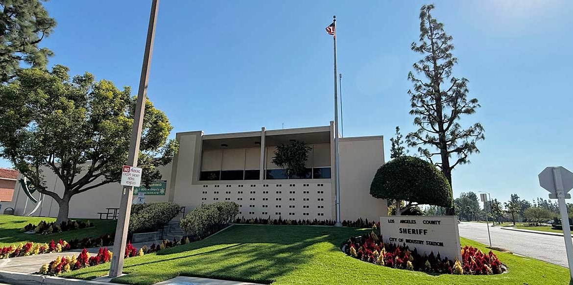 Los Angeles County Sheriff's Department Industry Station. White brick building with a green front lawn and red and orange flower beds in front.