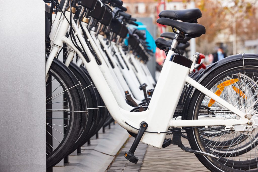 image of an e-bike charging station. rectangular metal box: white electric bikes are charging side by side.