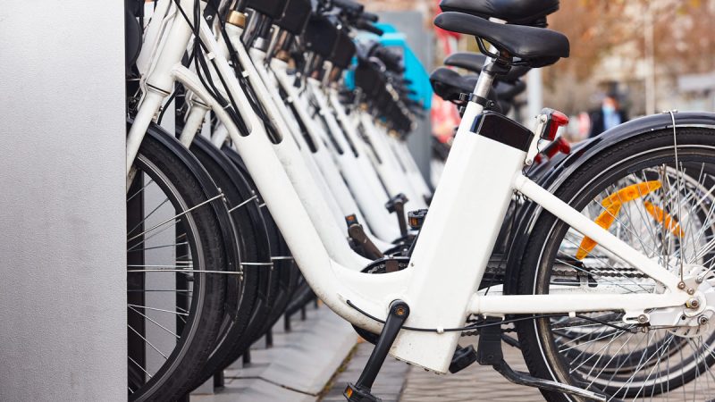 image of an e-bike charging station. rectangular metal box: white electric bikes are charging side by side.