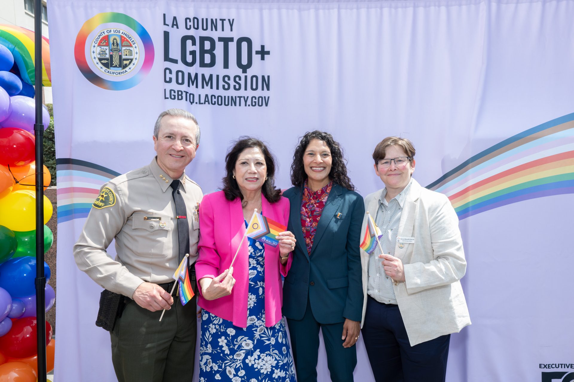 4 representatives posing infront of a flag, LA county LGBTQ commission.