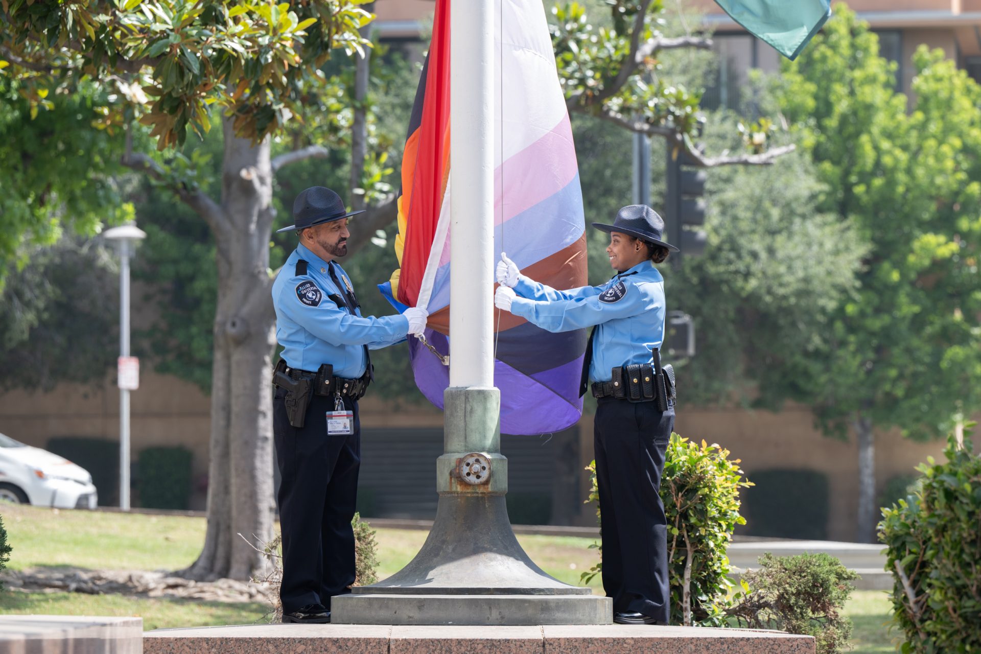 Two uniformed people are Raising the pride flag.