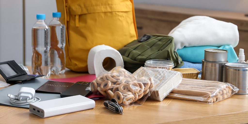 supplies and a yellow backpack displayed on a table. Charger, battery pack, bagged food and clothes.