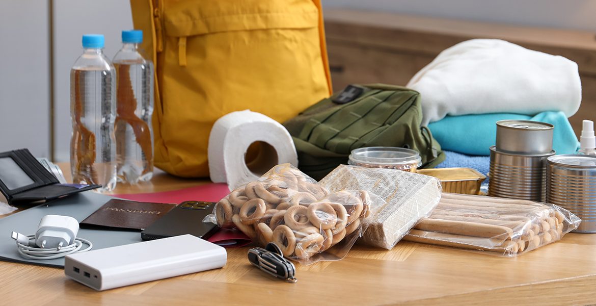 supplies and a yellow backpack displayed on a table. Charger, battery pack, bagged food and clothes.